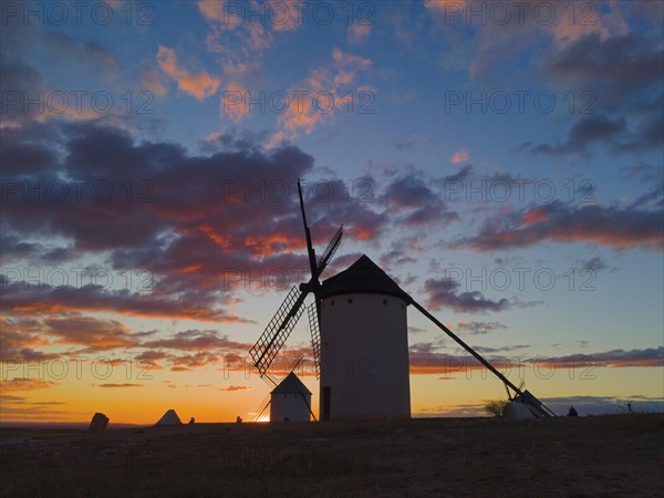 Windmills at dusk, silhouettes of buildings stand out against the colourful sky and scattered