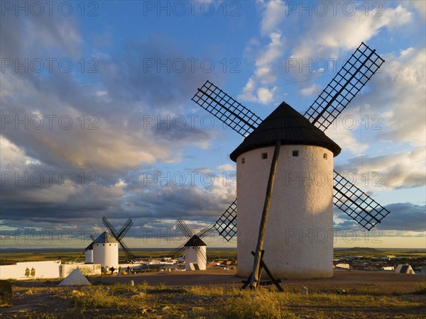 Several windmills in an open landscape, illuminated by sunlight, under a cloudy sky, windmills,