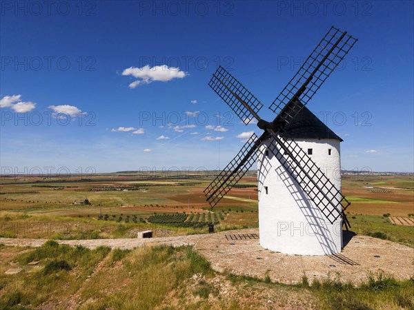 A single white windmill stands on a grassy field under a blue sky with few clouds, aerial view,