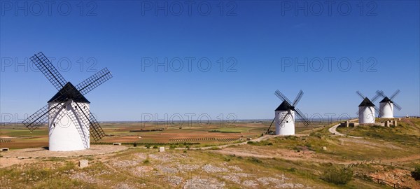 Several white windmills spread across a vast agricultural area under a clear blue sky, aerial view,