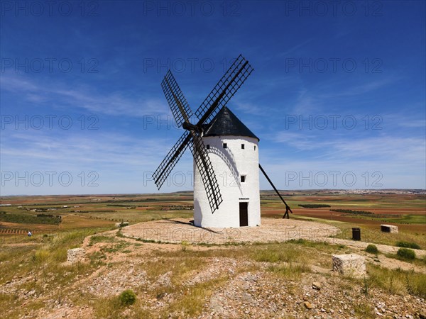 A lone white windmill stands in a field under a bright blue sky, aerial view, Alcazar de San Juan,