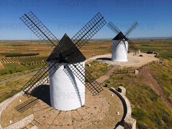 Two white windmills with black roofs in a wide field landscape in sunny weather, aerial view,