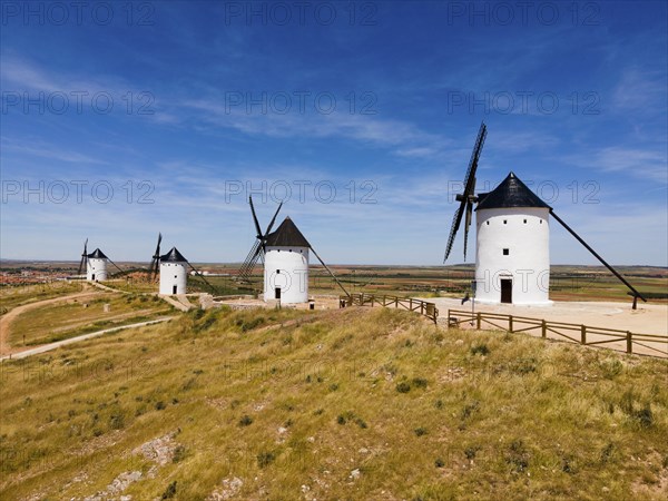 Several white windmills with black roofs in a vast scenic landscape under a clear blue sky, aerial