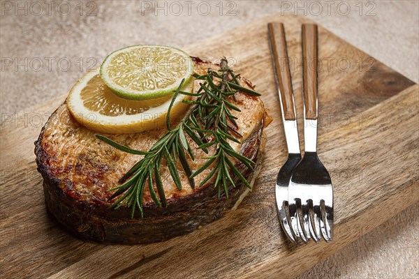 Salmon steak, fried, on a cutting board, top view, rosemary, lemon and lime, homemade, one serving,
