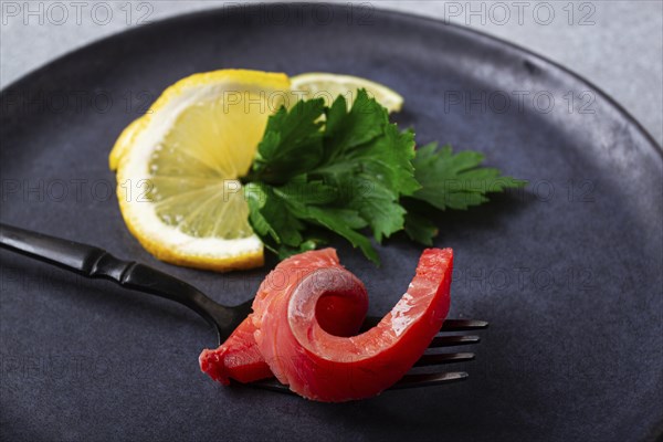 Chum salmon, cold smoked, on a fork, with lemon and parsley, top view, close-up, no people