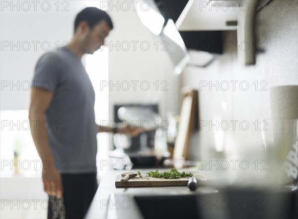 Cooking theme. A chopping board with parsley, in the background a man stands at the cooker and
