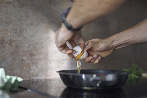 Cooking topic. A man cracks a raw egg into a pan. Berlin, 01.08.2024