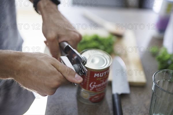 Cooking topic. A man opens a tin of tomatoes. Berlin, 01.08.2024