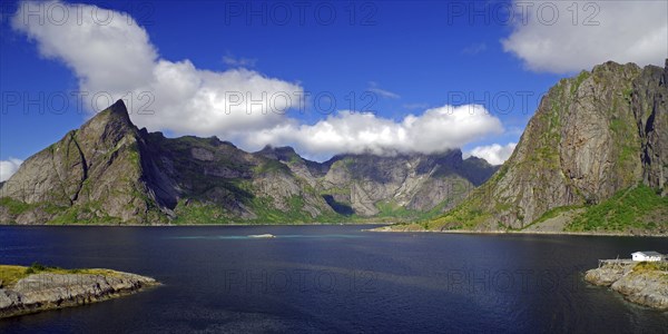 Impressive mountains under a blue sky with white clouds next to a calm fjord, Reinefjord, Hamnoy,