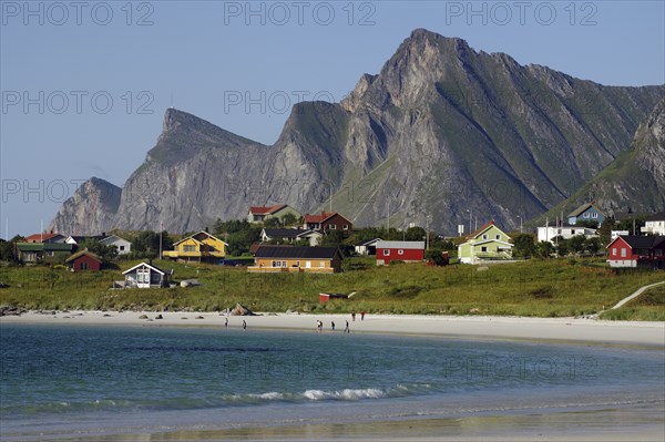Small coastal village with colourful houses and beach, framed by majestic mountains under a clear