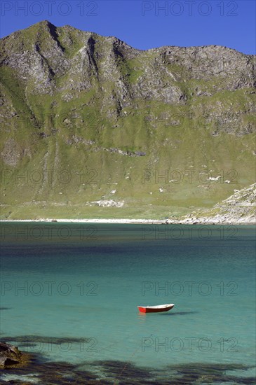 A red boat floats in a turquoise-coloured lake in front of a mountainous landscape, Haukland,