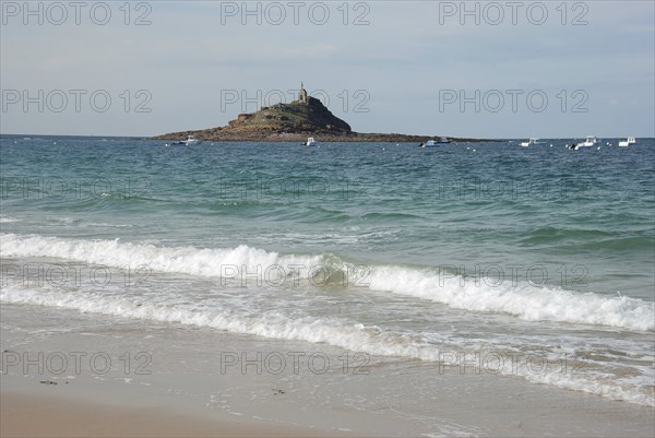 A lighthouse standing on an island surrounded by the ocean, with waves crashing on a sandy beach