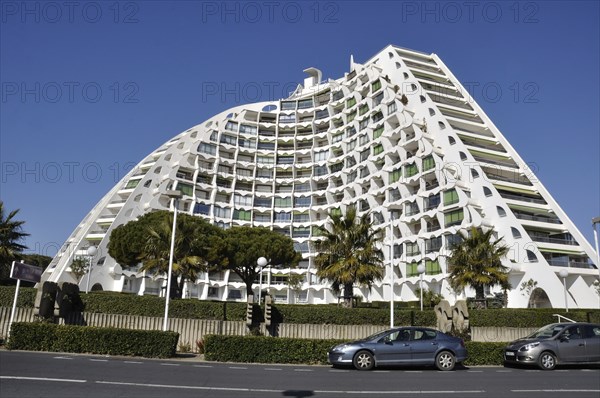 A modern curved building with a white facade and numerous balconies, set in an urban environment