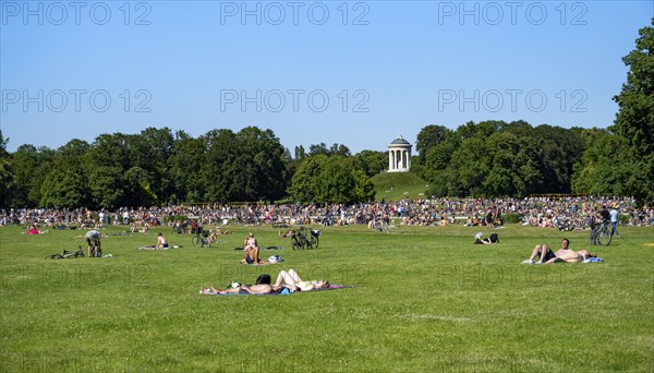 Many people in a meadow in the English Garden, people enjoying the summer day in the park behind