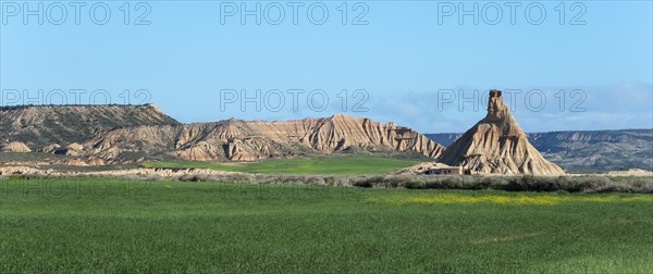 A unique rock formation rises in a green and dry landscape under a clear sky, rock formation under