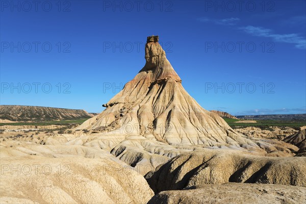 An impressive rock formation rises up in the desert-like landscape under a clear blue sky,