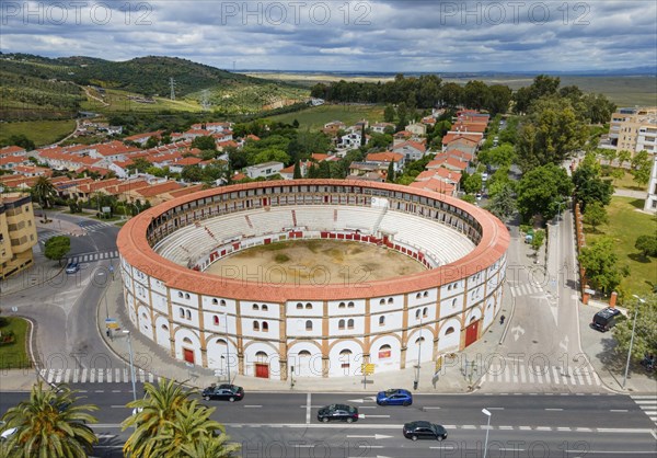 Aerial view of a historic bullring with red roofs in the middle of a city, surrounded by green