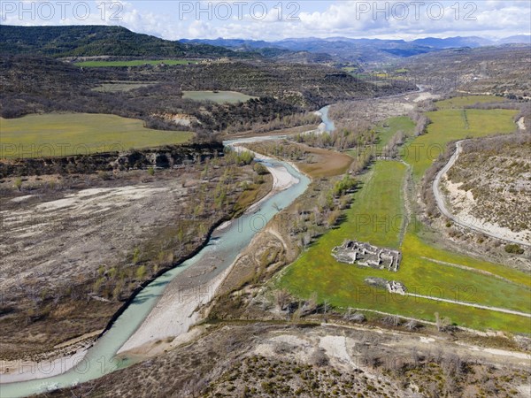 Aerial view of a river winding through a green meadow and past ancient ruins in the valley,
