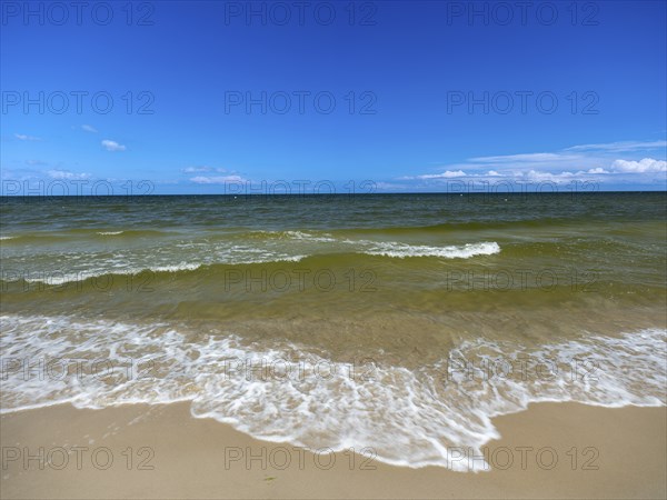 Water flowing onto the sandy beach on the island of Usedom on the Baltic Sea under a blue sky with