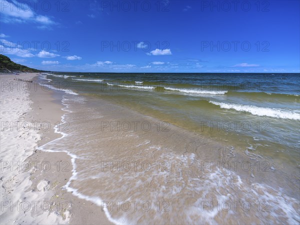 Water flowing onto the sandy beach on the island of Usedom on the Baltic Sea under a blue sky with