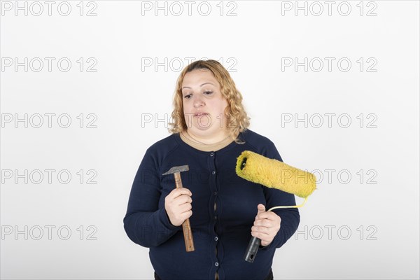 Woman looking confused at a paint roller and hammer