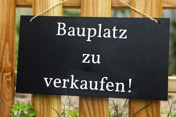 Sign with the inscription BAUPLATZ ZU VERKAUFEN on a wooden fence (symbolic image)