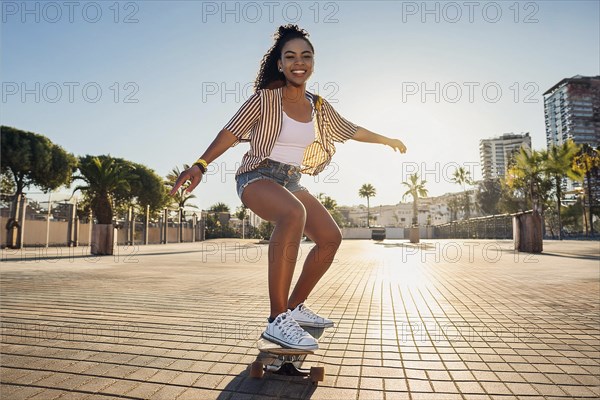Young woman enjoying a skateboard ride on a sunny day in a city with palm trees, ai generated, KI