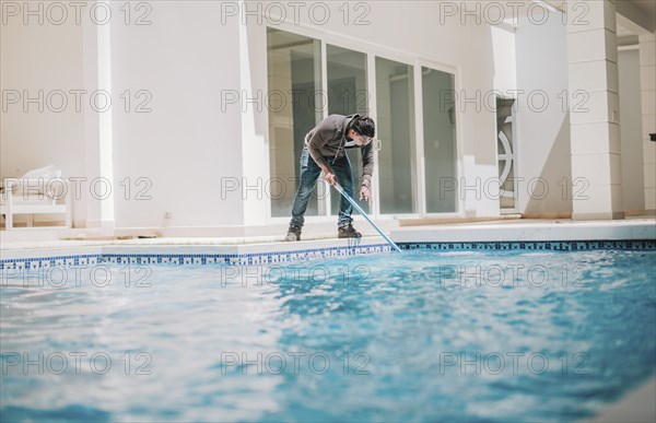 Person cleaning crystal clear pool with special brush. Home pool cleaning with wall brush