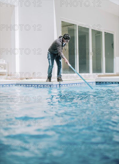 Young man cleaning a swimming pool with suction hose. Swimming pool cleaning and maintenance
