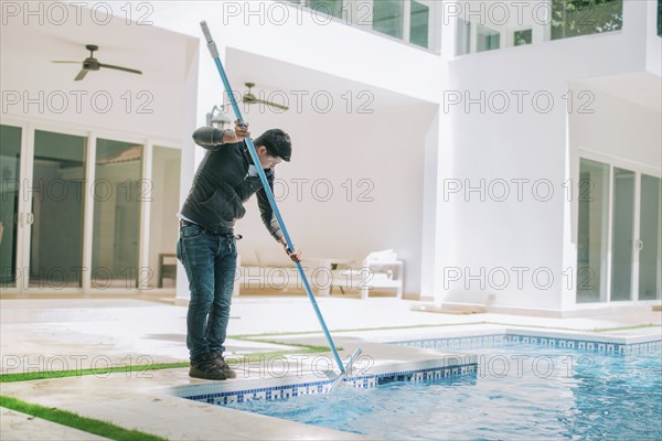 Person cleaning swimming pool with special brush. Maintenance person cleaning home pool with broom
