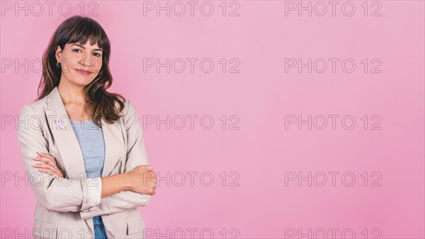 Smiling woman wearing a pink breast cancer awareness ribbon on her coat. Copy space