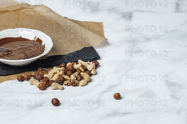 Chocolate icing in white bowl on baking paper, nut mixture, copy space