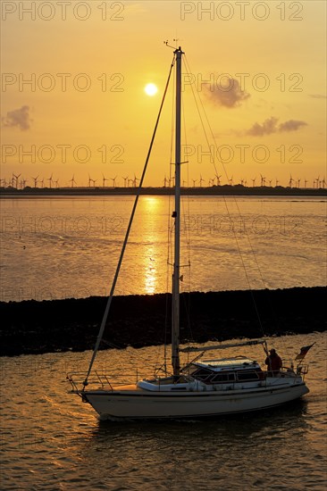 Sailboat on the North Sea at sunrise in front of mudflats and wind turbines, Norddeich, East