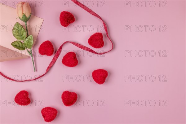 Romantic Valentine's Day scene with rose, envelope and red hearts on a pink surface