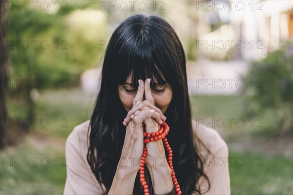 Woman practicing meditation sitting in yoga asana Kali Mudra holding a japa mala outdoors