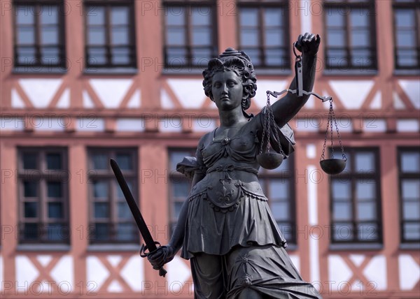 Justitia, Roman goddess of justice, with scales but without blindfold, in front of half-timbered
