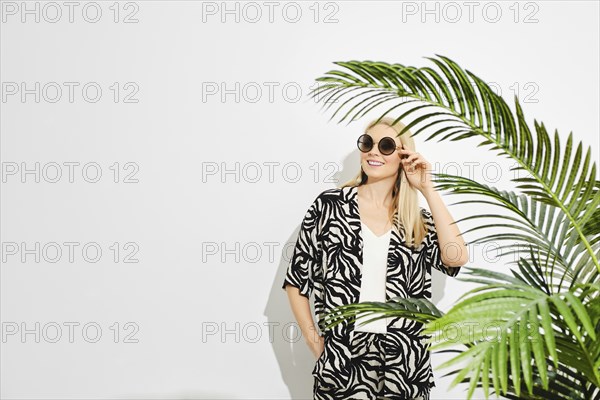 Happy woman stands by vibrant green palm leaves, creating a sense of mystery and connection with