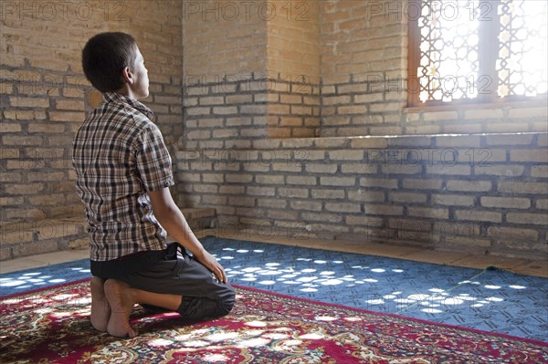 Praying Turkmen boy sitting on his knees in front of window in old Mosque in the ancient city of