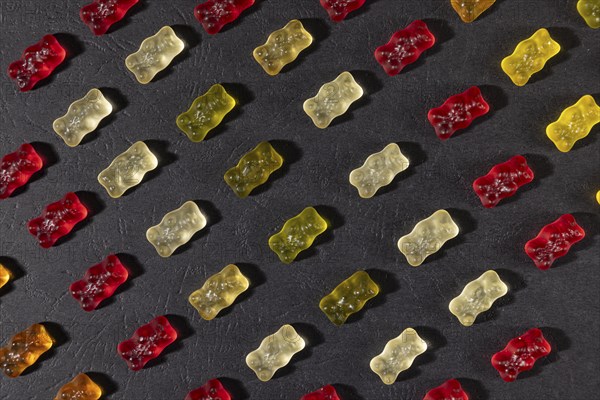 Different coloured gummy bears in rows, on a dark background
