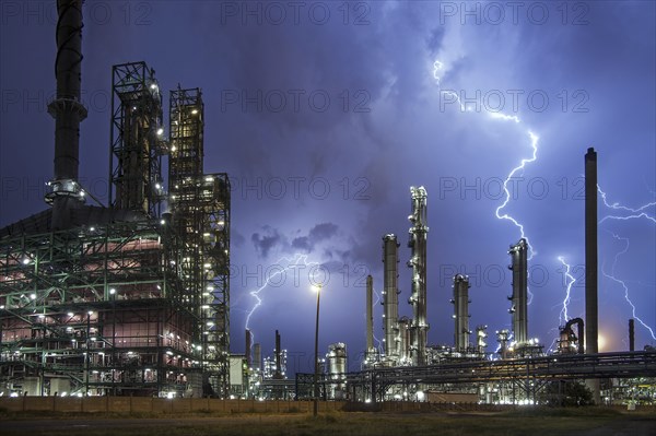 Lightning bolts striking over oil refinery at industrial estate during heavy thunderstorm at night,