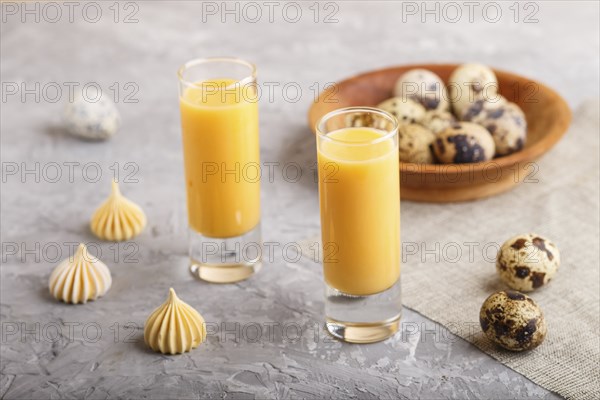 Sweet egg liqueur in glass with quail eggs and meringues on a gray concrete background. Side view,