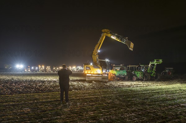 Man taking photos of excavators and tractors at a rally of farmers and peasants against the German
