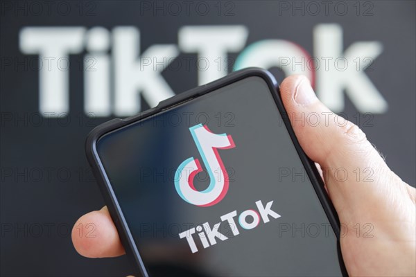 Hand holding mobile phone with TikTok logo social media with computer screen