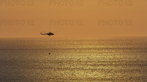 Helicopter, helicopter, fire-fighting helicopter, close over the sea, sunset, sun reflections on