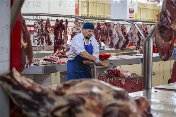 Man chopping meat and bones, butcher's shop with fresh meat, market at Osh bazaar, Bishkek,