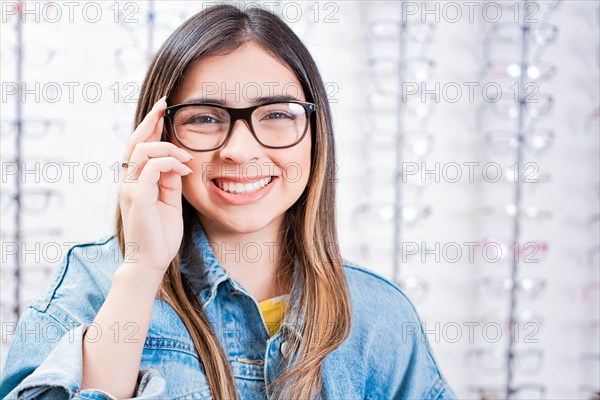 Smiling beautiful girl modeling glasses in an optical store. Happy teen girl in eyeglasses with