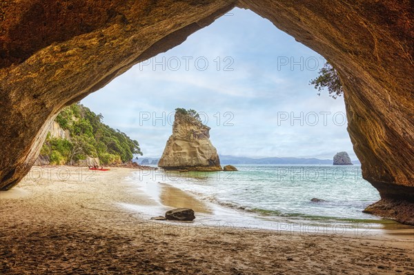 View from a cave onto a beach and isolated rocks in the sea, under a cloudy sky, Cathedral Grove,