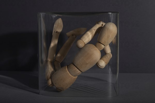 Wooden mannequin locked in a glass cube on gray background. captivity, break rules, loneliness,