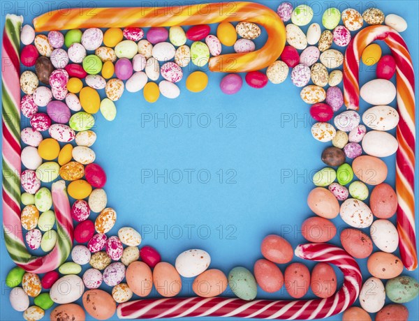 Colorful frame of multicolored candies on a blue background. Christmas cane, chocolate eggs,