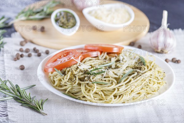 Spaghetti pasta with pesto sauce, tomatoes and cheese on a linen tablecloth. close up, selective